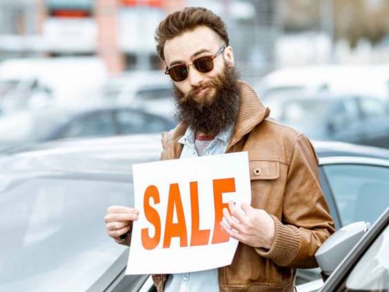 Stylish bearded salesman with sales plate near cars in the open area of ​​a dealership