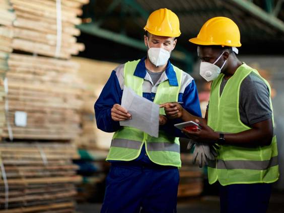 Two manual workers with face masks going though checklist while working in timber warehouse.