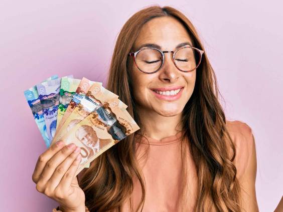Young brunette woman holding canadian dollars screaming proud, celebrating victory and success very excited with raised arm