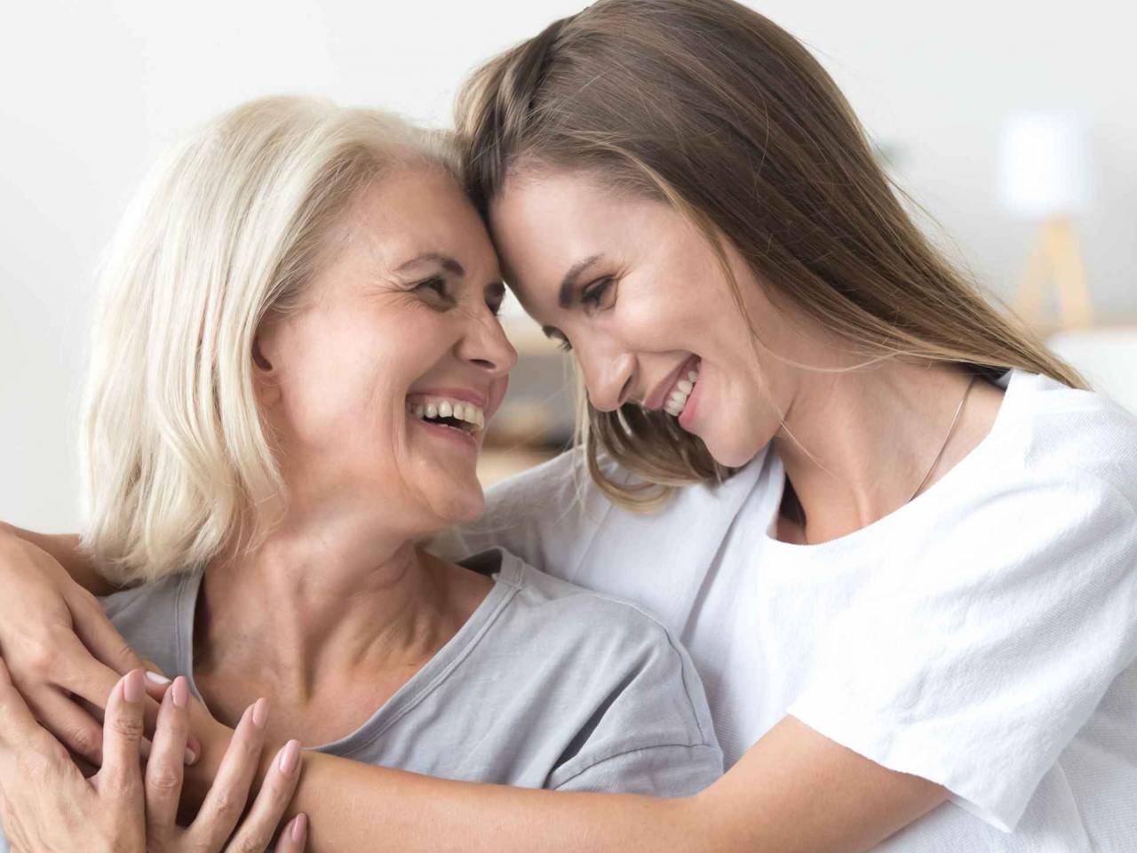 Happy loving older mature mother and grown millennial daughter laughing embracing, caring smiling young woman embracing happy senior middle aged mom having fun at home spending time together