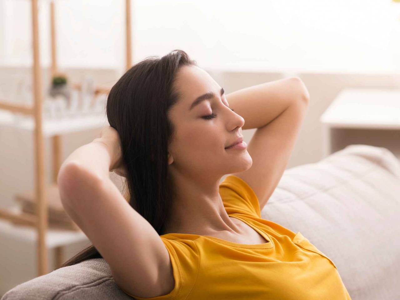 Keep calm and stay home. Peaceful young woman relaxing on sofa in living room