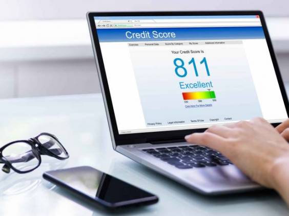 Person using laptop to check credit score with phone and glasses placed next to computer.