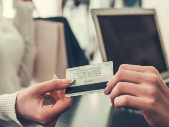 Attractive girl gives seller credit card and smiles while shopping in boutique