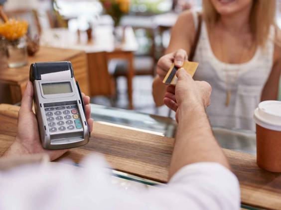 Customer paying for their order with a credit card in a cafe. Bartender holding a credit card reader machine and returning the debit card to female customer after payments.