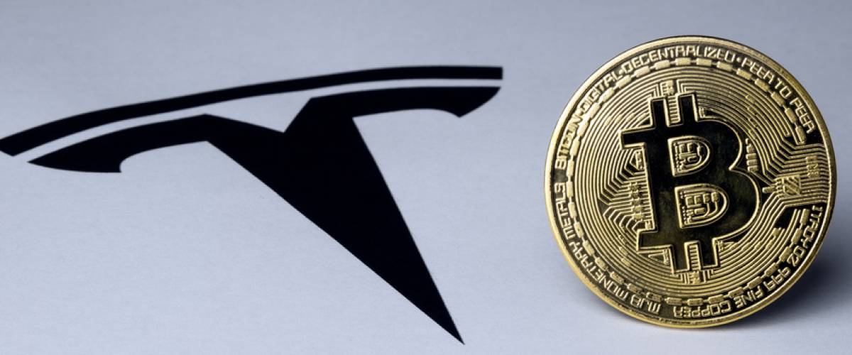 Bitcoin and Tesla logo seen on paper document. Concept for investment in cryptocurrency.