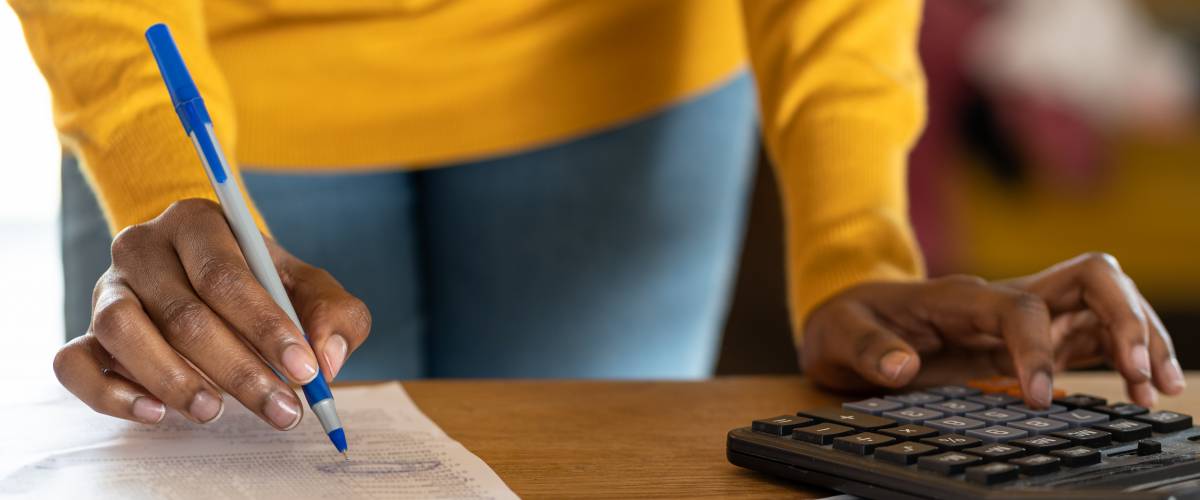 close up of woman of color using calculator, holding pen, writing note with calculate