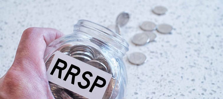 Hand holding glass jar with many coins and RRSP word over a marble counter top.Canadian Registered Retirement Savings fund concept.