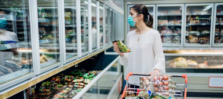 Woman wearing face mask buying in supermarket.Panic shopping during Coronavirus covid-19 pandemic.Budget buying at a supply store.Buying freezer smart purchased household pantry groceries