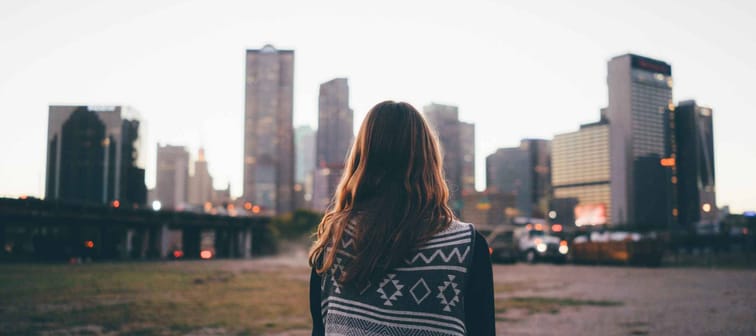 A traveler brunette girl is looking at the city skyline during in the evening.