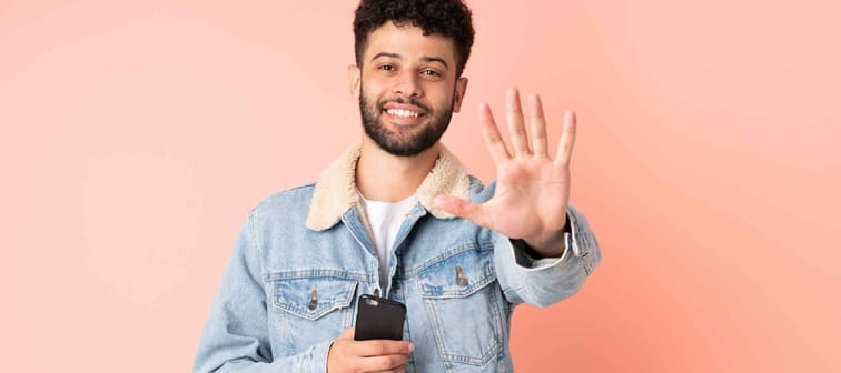 Young Moroccan man using mobile phone isolated on pink background counting five with fingers