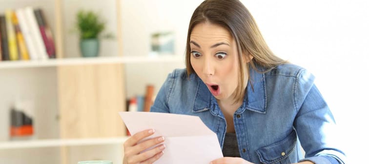 Amazed woman reading surprising news in a letter sitting in a desktop at home