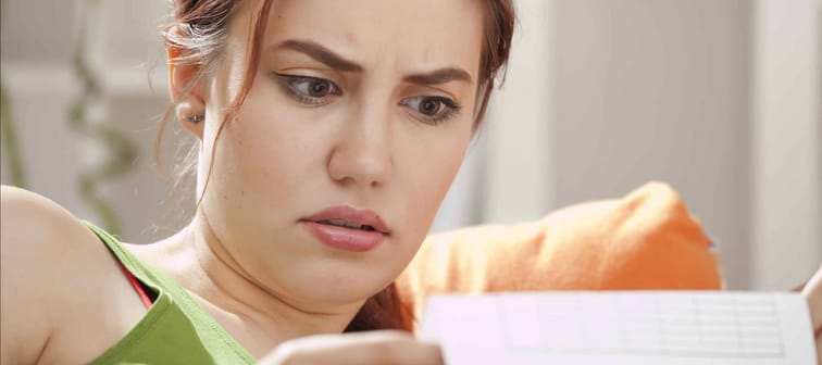 Shocked young woman looks at document at home