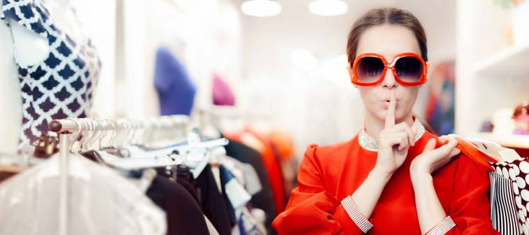 Woman with finger over her lips, wearing sunglasses in a clothing store