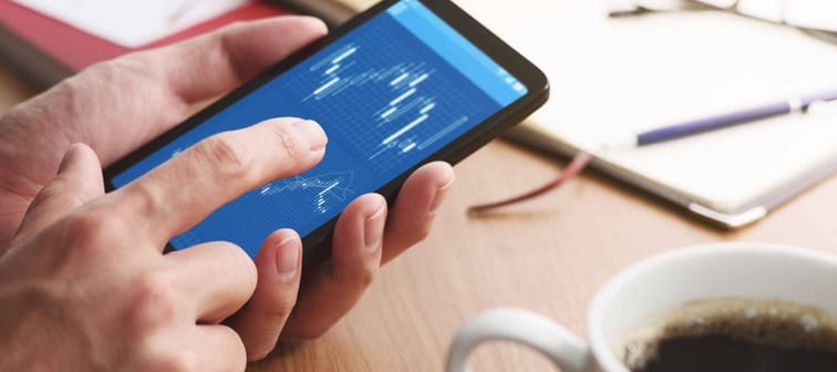 Stock market charts on smartphone screen.Closeup of male hands holding smartphone. Checking financial market.