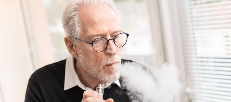 Older man takes a puff of an e-cigarette.