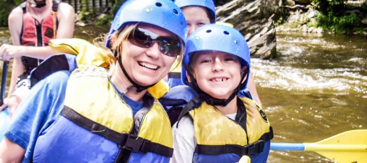 Mom and kids smile at camera while wearing helmets, life jackets in a boat.