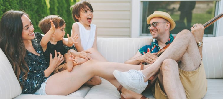Happy young family sitting out on patio furniture on a sunny day, singing and playing.