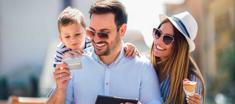 Smiling parents and little girl with tablet pc and credit card outdoor