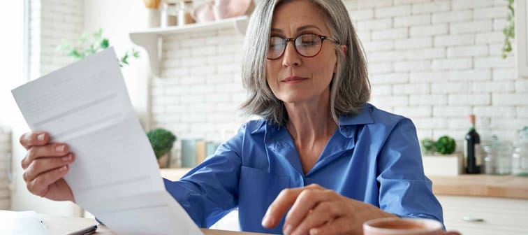 Senior mature business woman holding paper bill using calculator.