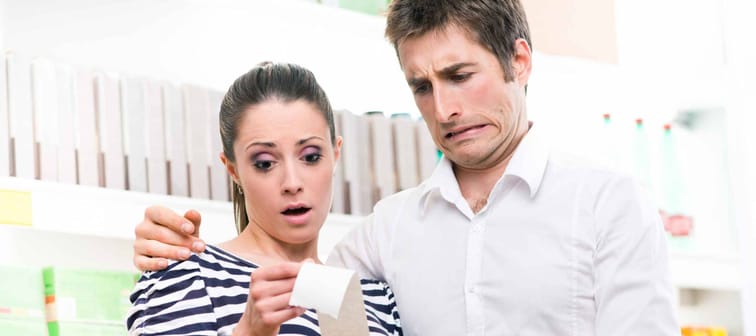 Young astonished couple checking a long grocery receipt at supermarket.