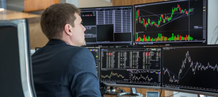 Businessman trading stocks. Stock traders looking at graphs, indexes, numbers and analyses on multiple computer screens in modern trading office.