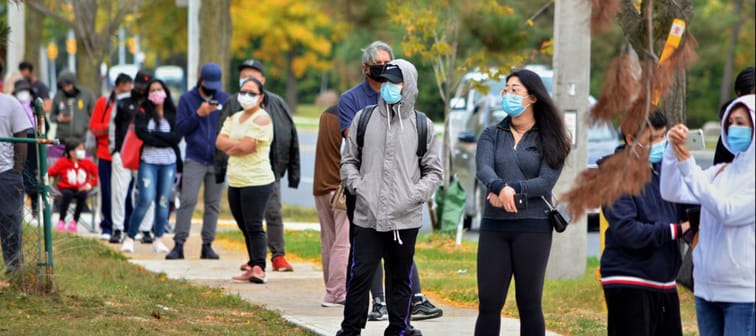 People wearing masks wait in line on the sidewalk to get a COVID test