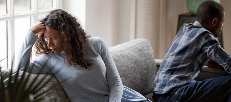 Depressed mixed race couple sit separate on couch having relationships problems
