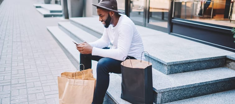 Man sitting on stairs with shopping bags and phone in hand