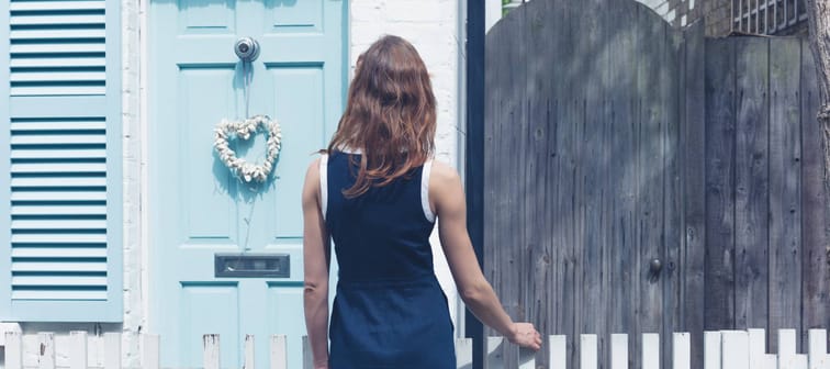 A young woman is looking at a little house with a blue door